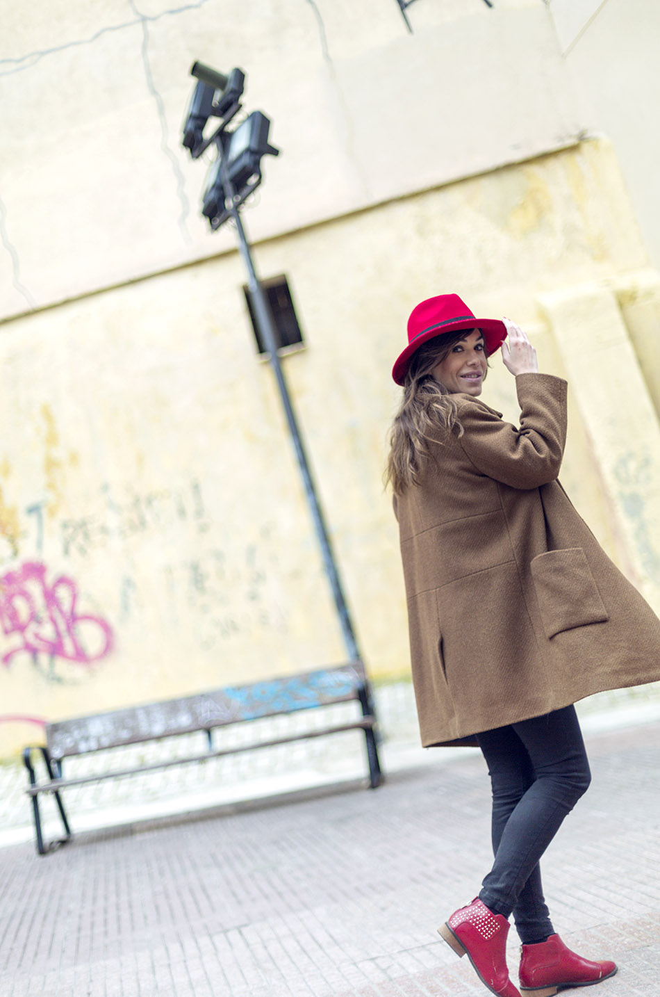look de street style con abrigo marrón de lana, top de lunares  estilo naif, jeans pitillos, botines rojos y sombrero rojo