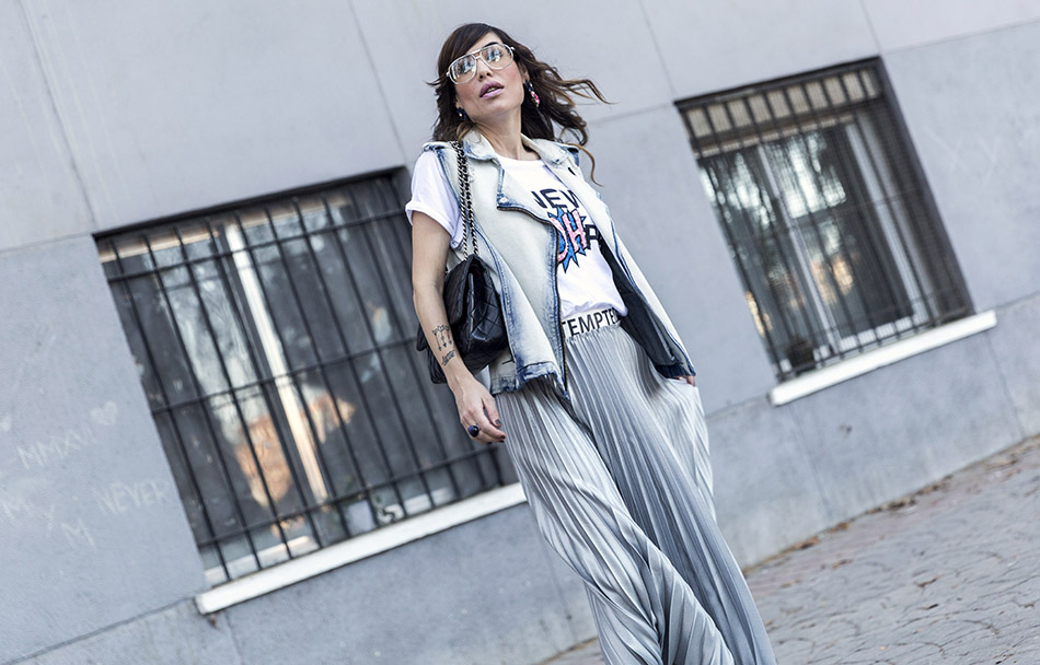 look de street style con chaleco vaquero, camiseta de Mango con texto New York, falda plisada de color plata, zapatos de salon azules y bolso plateado