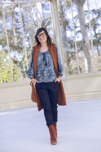 look de street style con chaleco de lana en color caramelo, blusa con print de paisley, pantalones de vestir azules y botines de ante en color caramelo