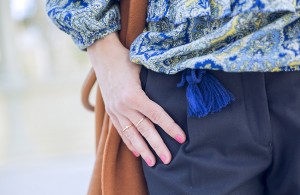 look de street style con chaleco de lana en color caramelo, blusa con print de paisley, pantalones de vestir azules y botines de ante en color caramelo