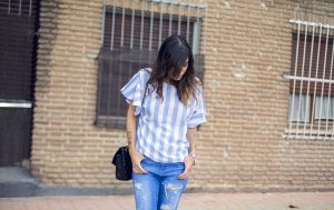 look de street style con top de rayas verticales azules y blancas y coolants en las mangas, jeans pitillos desgastados, sandalias planas tipo bailarina y bolso de Chanel