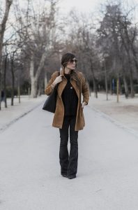 look de street style con abrigo tipo levita de ante en color camel, jersey negro con detalle de flores bordadas y flared jeans