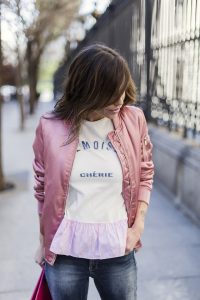 look de street style con camiseta blanca con mensaje y detalle de volante rosa en el bajo, pantalones jeans pitillos, botines plateados y bomber rosa